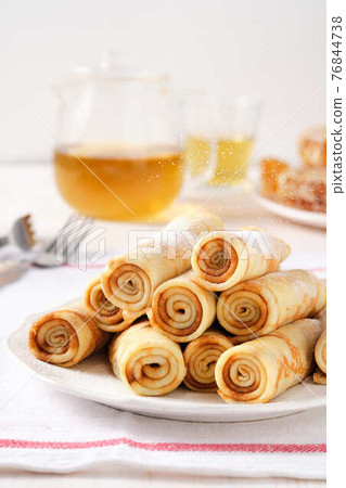 Crepes, thin pancakes with honey and tea on a white plate. 76844738