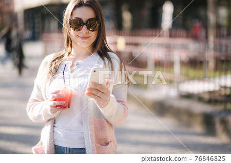 Beautiful woman using phone and drinks lemonade outdoor. Young blogger spend time in park 76846825