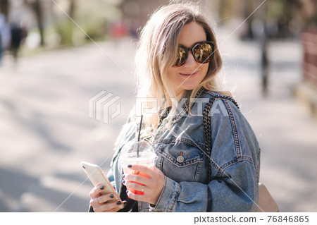 Pretty prengant woman dringking strawberry lemonade while walking outdoors. Portrair of attractive female in sunglasses using phone 76846865