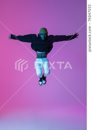 Young stylish man in modern street style outfit isolated on gradient background in neon light. African-american fashionable model in look book, musician performing. Young stylish man in modern street style outfit isolated on gradient background in neon light. African-american fashionable model in look book, musician performing. 76847035