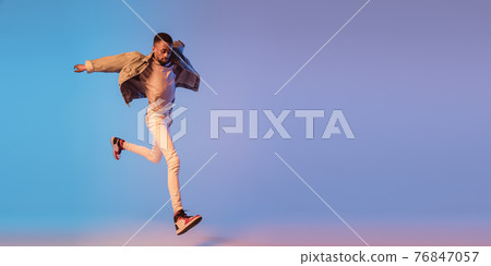 Young stylish man in modern street style outfit isolated on gradient background in neon light. African-american fashionable model in look book, musician performing. 76847057