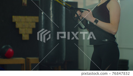 Blonde woman in sportswear doing exercise with TRX system at gym. Cross training. Modern fitness. 76847832