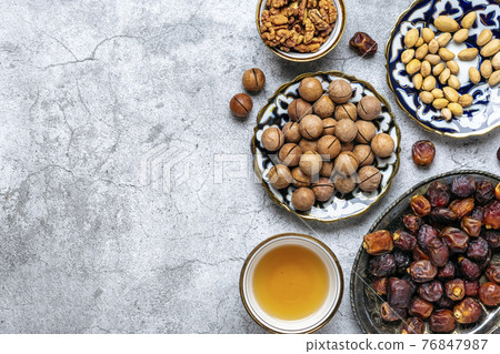 Popular food during Iftar - macadamia nuts, pistachios, walnuts, dry dates. Karan, rosary, teapot, bowl with black tea on concrete background Top view Flat lay Muslim holiday of holy month of Ramadan 76847987