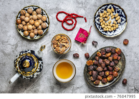Popular food during Iftar - macadamia nuts, pistachios, walnuts, dry dates. Karan, rosary, teapot, bowl with black tea on concrete background Top view Flat lay Muslim holiday of holy month of Ramadan 76847995