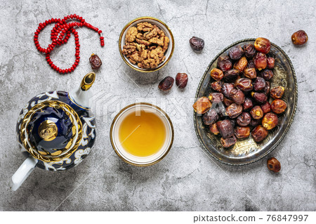 Popular food during Iftar - macadamia nuts, pistachios, walnuts, dry dates. Karan, rosary, teapot, bowl with black tea on concrete background Top view Flat lay Muslim holiday of holy month of Ramadan 76847997