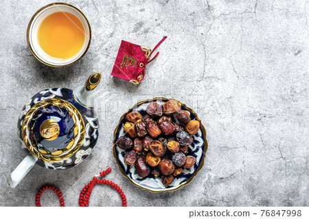 Popular food during Iftar - macadamia nuts, pistachios, walnuts, dry dates. Karan, rosary, teapot, bowl with black tea on concrete background Top view Flat lay Muslim holiday of holy month of Ramadan 76847998