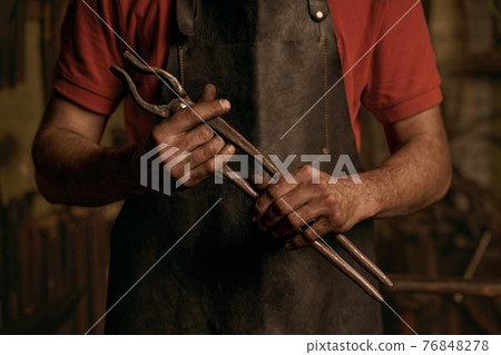 Blacksmith with metal tongs in smithy portrait Blacksmith with metal tongs in smithy portrait 76848278