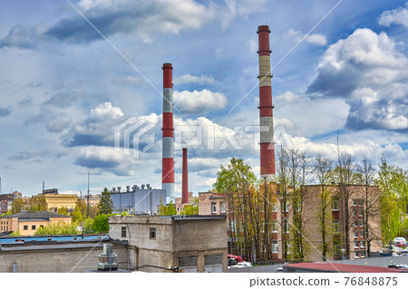 Tall factory chimneys against backdrop of a cloudy sky and residential buildings 76848875