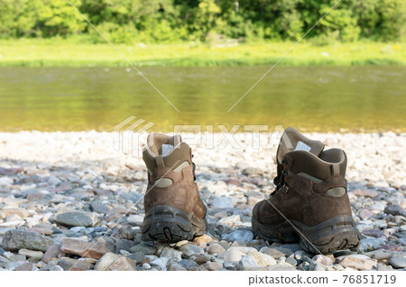 The choice of shoes for tourism and trekking. Brown boots stand on a stony bank outdoor. back view 76851719