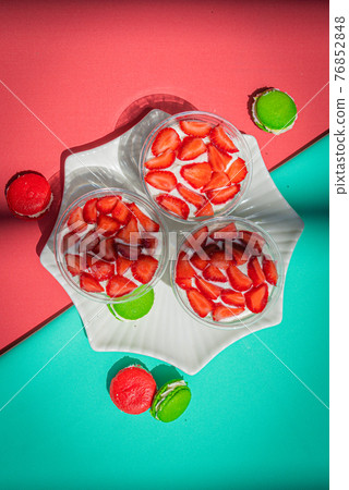 Strawberries in yogurt on a plate and french macarons on a bright abstract background. 76852848