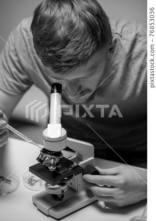 young bearded biologist looking through microscope examining seeds of plants young bearded biologist looking through microscope examining seeds of plants 76853036