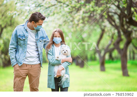 Family of father and daughter in blooming cherry garden in masks 76853902