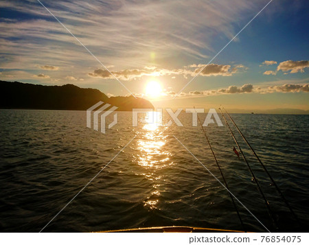 Silhouette of the rising sun and fishing rod from the other side of the sea Silhouette of the rising sun and fishing rod from the other side of the sea 76854075
