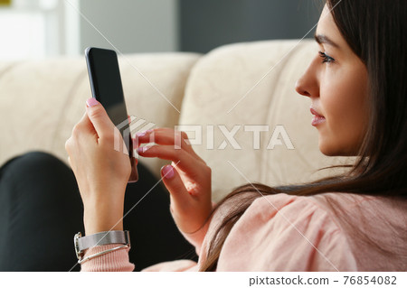 Lonely woman is sitting on couch and looking into smartphone Lonely woman is sitting on couch and looking into smartphone 76854082