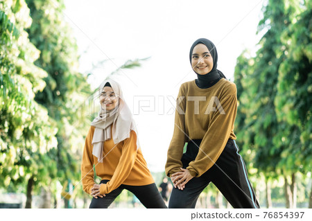 beautiful two Muslim girls in headscarves do lunges movement before outdoor sports beautiful two Muslim girls in headscarves do lunges movement before outdoor sports 76854397