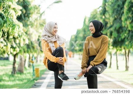 two girls in veil stretching their leg muscles by lifting and holding the bent leg with their arms before jogging 76854398