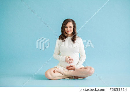 Pretty pregnant woman doing Padmasana or The Lotus Pose on blue background 76855814