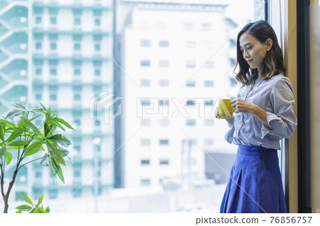 A woman drinking coffee by the window of a building office 76856757