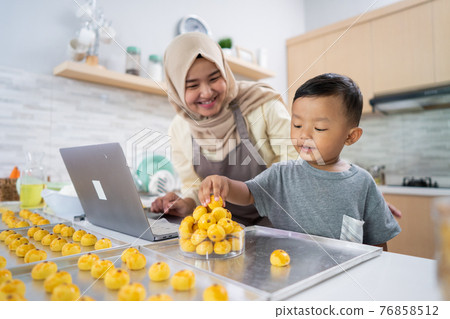 muslim mother looking at laptop while making cake with her son in the kitchen muslim mother looking at laptop while making cake with her son in the kitchen 76858512