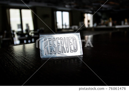 Metal plaque Reserved on a black table in a cafe against a background of blur and light in the windows. 76861476