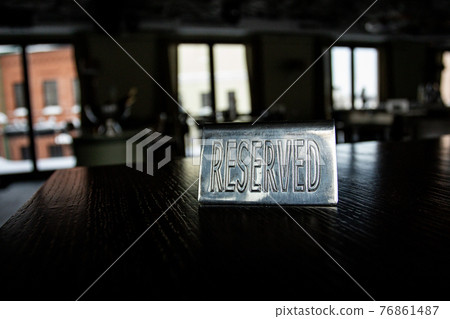 Metal plaque Reserved on a black table in a cafe against a background of blur and light in the windows. Metal plaque Reserved on a black table in a cafe against a background of blur and light in the windows. 76861487