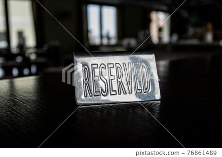 Metal plaque Reserved on a black table in a cafe against a background of blur and light in the windows. Metal plaque Reserved on a black table in a cafe against a background of blur and light in the windows. 76861489