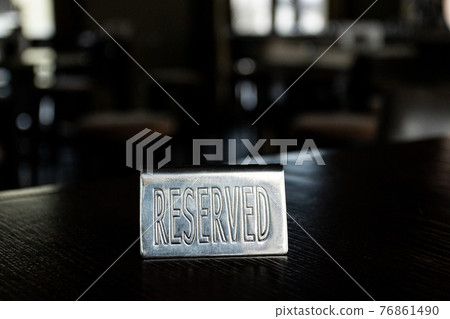 Metal plaque Reserved on a black table in a cafe against a background of blur and light in the windows. 76861490