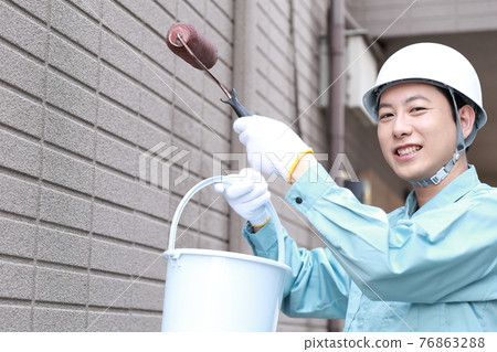 Male worker painting the exterior walls of a house 76863288