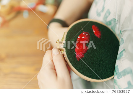 Girl is embroidering mushroom cap on green cloth. Girl is embroidering mushroom cap on green cloth. 76863937