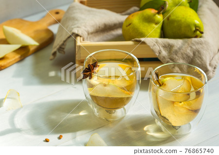 Two glasses of refreshing pear cider on a wooden table, lit by the sun from the window. A small box with pears in the background 76865740