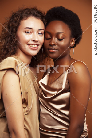 two pretty girls african and caucasian blond posing cheerful together on brown background, ethnicity diverse lifestyle people concept two pretty girls african and caucasian blond posing cheerful together on brown background, ethnicity diverse lifestyle people concept 76866190