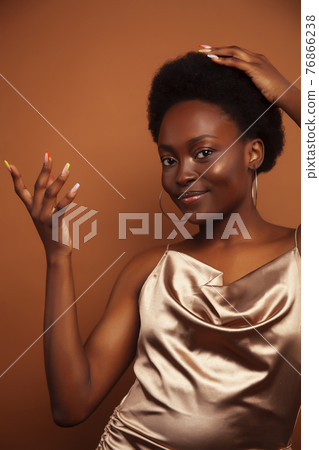 pretty young african american woman with curly hair posing cheerful gesturing on brown background, lifestyle people concept 76866238