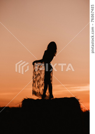 Silhouette of a sexy girl in a transparent dress in summer at sunset in a field 76867485