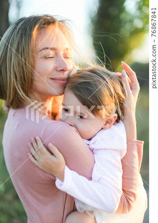 Portrait of young mother hugging little daughter and smiling. 76867841