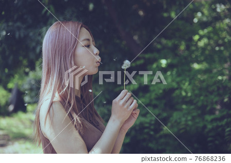 Portrait of a beautiful woman blowing dandelion fluff 76868236