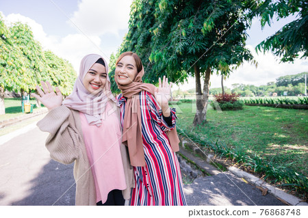 Muslim women in hijabs outdoors on sunny day with friend happy 76868748