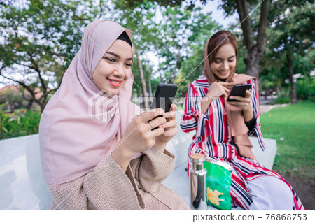 muslim woman in head scarf meet friends and using phone in the park 76868753