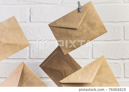 Concept postal communication background, several new paper brown craft letter envelopes hang on clothespins on a rope against a white wall background Concept postal communication background, several new paper brown craft letter envelopes hang on clothespins on a rope against a white wall background 76868828