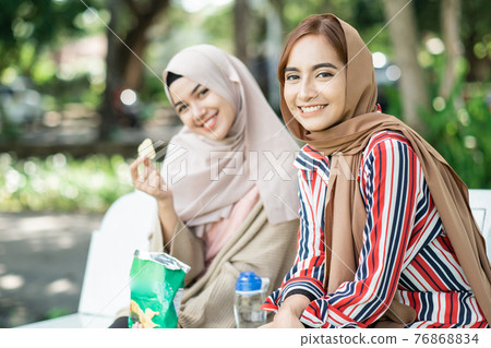 muslim young woman with friend enjoy their snack while relaxing in the park 76868834