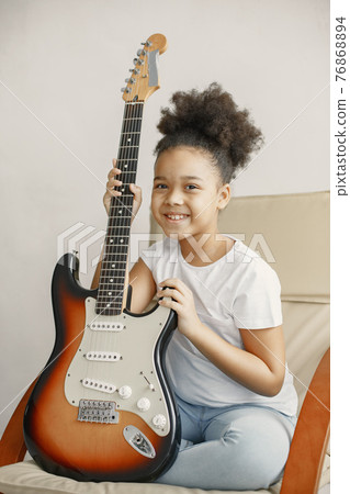 Little girl with a guitar on a chair Little girl with a guitar on a chair 76868894