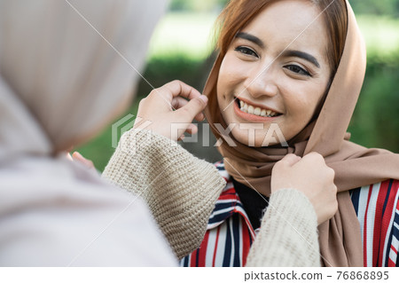 muslim asian woman fixing friend hijab while meeting outdoor muslim asian woman fixing friend hijab while meeting outdoor 76868895
