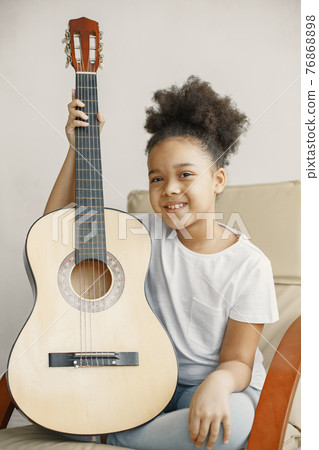 Little girl with a guitar on a chair Little girl with a guitar on a chair 76868898