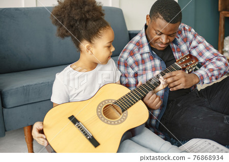 African father teaches his daughter to play guitar 76868934