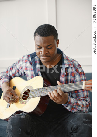 African man playing guitar while sitting on sofa 76868995