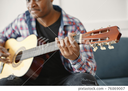 African man playing guitar while sitting on sofa 76869007