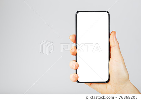 Hand holds black smartphone with blank white screen and modern frameless design isolated on gray background. 76869203