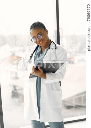 African doctor standing by window with a folder African doctor standing by window with a folder 76869270