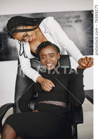 African American cheerful businesswomen at office desk in stylish suits African American cheerful businesswomen at office desk in stylish suits 76869275