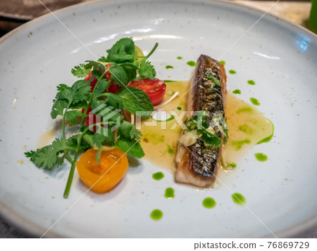 Pan fried mackerel fish with spicy dressing and tomato decorated on white dish in restaurant, selective focus Pan fried mackerel fish with spicy dressing and tomato decorated on white dish in restaurant, selective focus 76869729