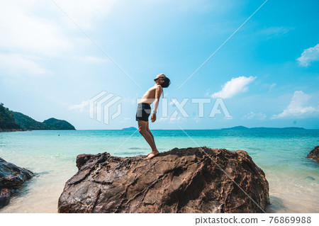 A man standing on a rock at the beach in summer A man standing on a rock at the beach in summer 76869988